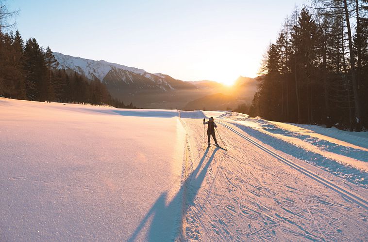 Langläufer bei Sonnenaufgang auf Loipe in der Region Seefeld, umgeben von verschneiten Bergen.