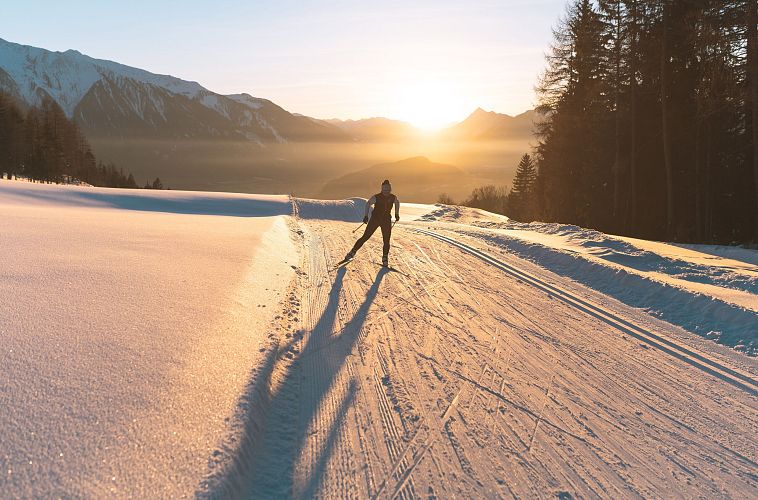 Langläufer bei Sonnenuntergang in der Region Seefeld, umgeben von Bergen und verschneiter Landschaft.