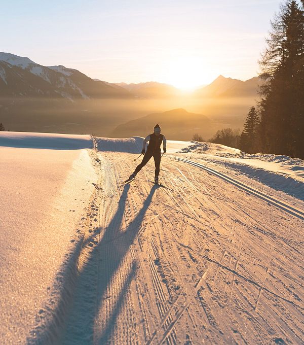 Langläufer bei Sonnenuntergang in der Region Seefeld, umgeben von Bergen und verschneiter Landschaft.