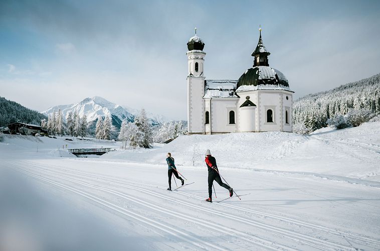 Langläufer vor Kirche in schneebedeckter Landschaft der Region Seefeld. Ideal zum Langlaufen.