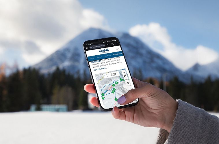 Smartphone zeigt Karte der Region Seefeld, Hintergrund mit verschneiten Bergen.