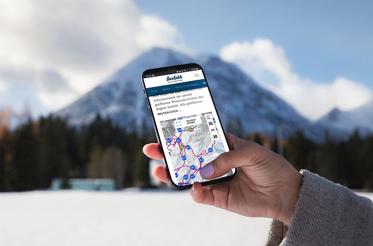 Person hält Smartphone mit Karte der Region Seefeld, schneebedeckter Berg im Hintergrund.