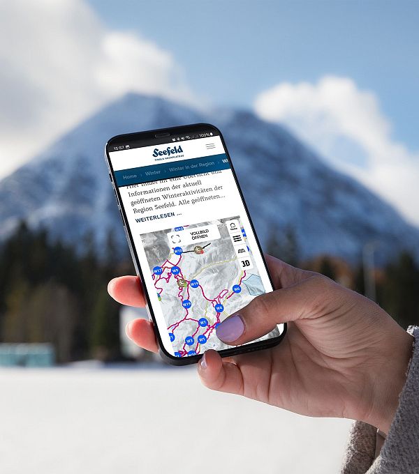 Person hält Smartphone mit Karte der Region Seefeld, schneebedeckter Berg im Hintergrund.
