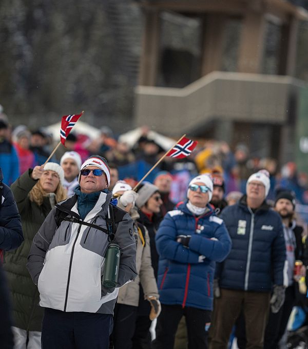 A crowd of spectators at a winter sports event, many wearing winter gear and holding flags.
