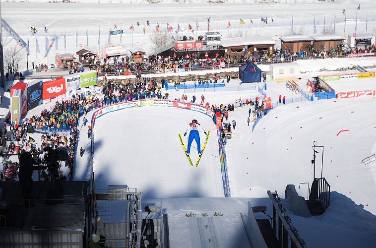 Nordic Combined Triple Seefeld 2025_Skispringer mit Seefeld Sports Arena und Zuschauern im Hintergrund