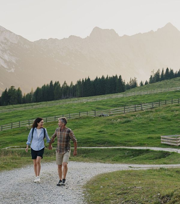 Paar geht Hand in Hand auf einem Weg in einer grünen Landschaft mit Bergen im Hintergrund.