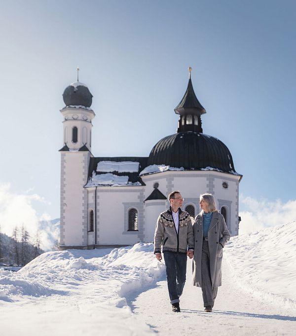 Paar geht im Schnee vor einer historischen Kirche spazieren.