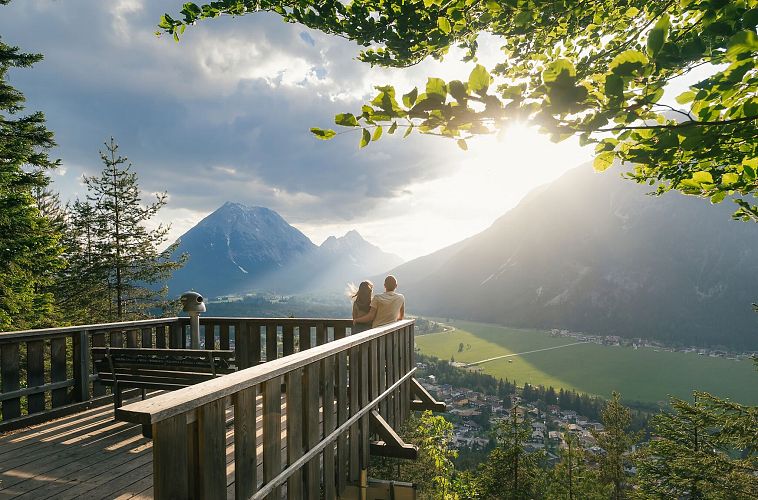 Zwei Personen auf einer Aussichtsplattform mit Blick auf Berge und Tal.