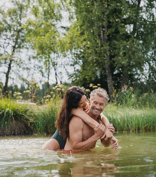 A couple embracing playfully in a pond surrounded by greenery.