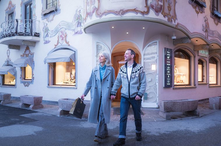 Paar geht shoppen in Seefeld im Winter_Aufnahme vor Armbruster_Frau hat Taschen in der Hand