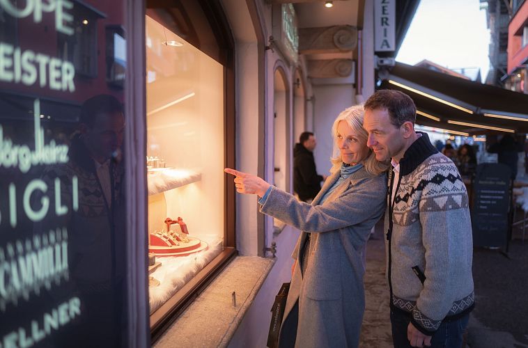 Ein älteres Paar betrachtet gemeinsam ein festlich dekoriertes Schaufenster in einer belebten Straße.