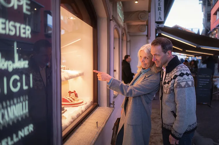 Paar geht shoppen in Seefeld im Winter_Paar steht am Schaufenster beim Armbruster_Frau zeigt auf etwas