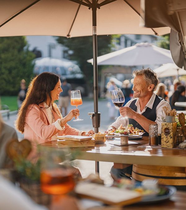 Zwei Personen in einem Freiluftrestaurant stoßen mit Getränken an.