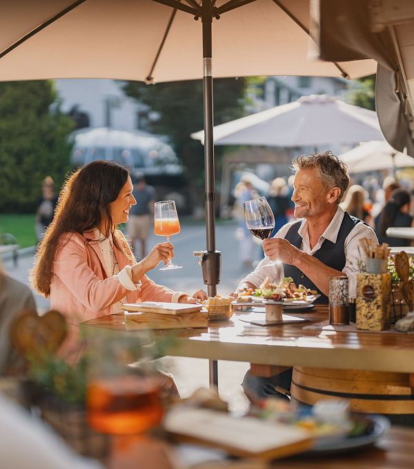 Zwei Personen in einem Freiluftrestaurant stoßen mit Getränken an.