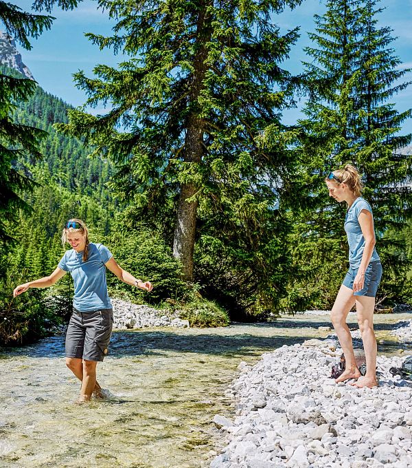 Zwei Kinder verbringen Zeit im Gebirgsfluss, umgeben von Bäumen und Bergen.
