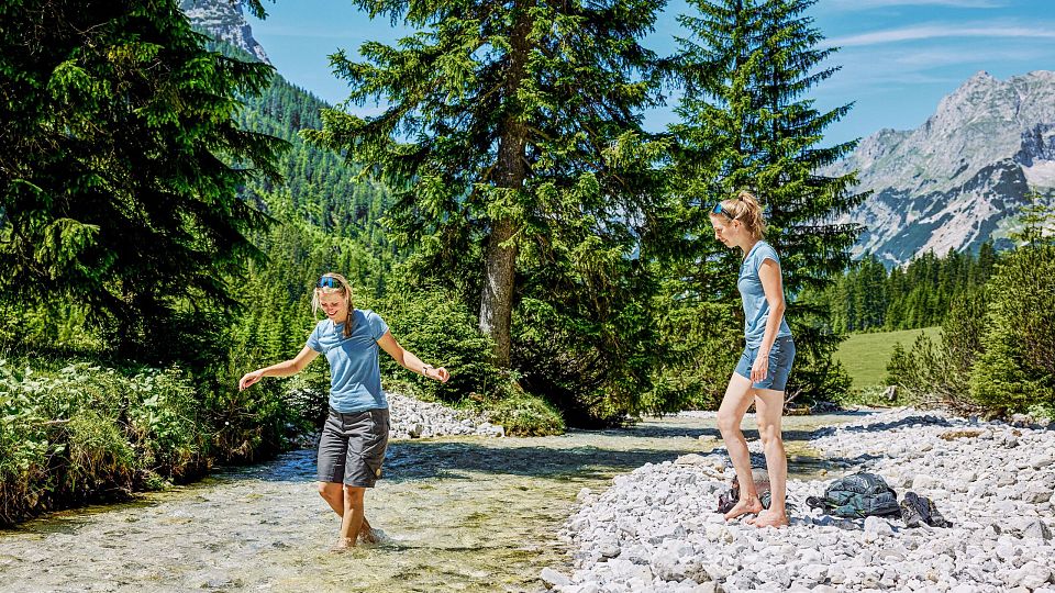 Zwei Kinder verbringen Zeit im Gebirgsfluss, umgeben von Bäumen und Bergen.