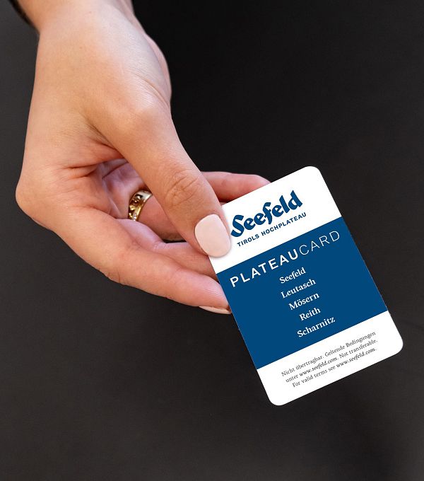 A hand holding a Seefeld Plateau Card with service details printed on it.