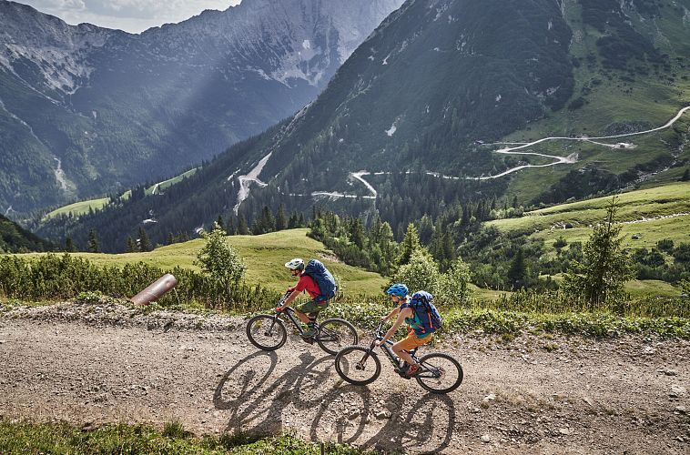 Zwei Radfahrer auf einem Pfad in der Berglandschaft der Region Seefeld. Im Hintergrund sieht man Berge und eine kurvige Straße.