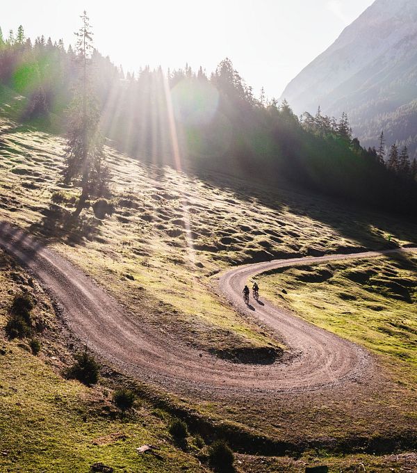 Wanderer auf einem sonnigen Bergpfad in der Region Seefeld, umgeben von grünen Wiesen und Bergen.