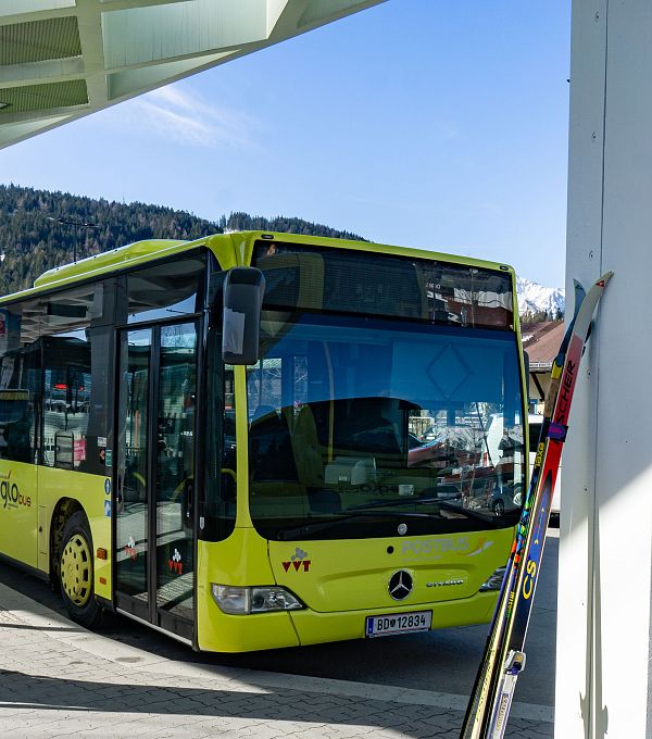 Gelber Linienbus der Marke Mercedes-Benz an einer Haltestelle mit Skiausrüstungen im Hintergrund.