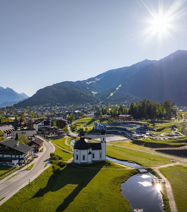 A panoramic view of a village surrounded by mountains and green terrain under a bright sun.