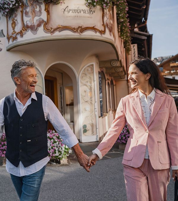 Lächelndes Paar spaziert durch blumengeschmückte Straße mit traditioneller Architektur.