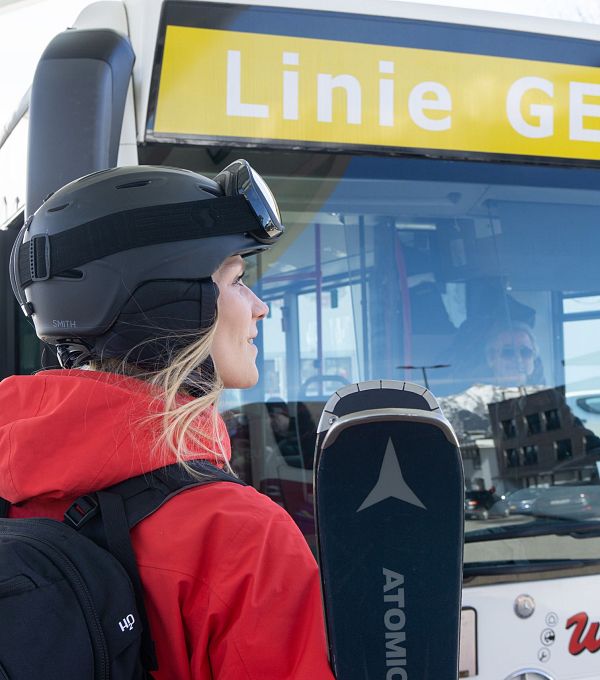 Eine Frau in Skikleidung steht vor einem Bus mit der Aufschrift 'Linie GELB'.