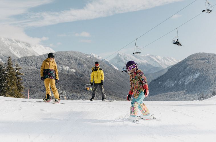 Winterlandschaft in der Region Seefeld. Kinder fahren Ski, Erwachsene beobachten. Sessellift und verschneite Berge im Hintergrund.