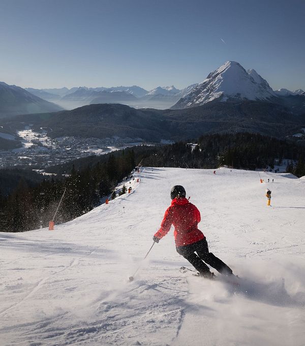 Ein Skifahrer in roter Jacke fährt die Piste hinunter, umgeben von Bergen und einer verschneiten Landschaft.