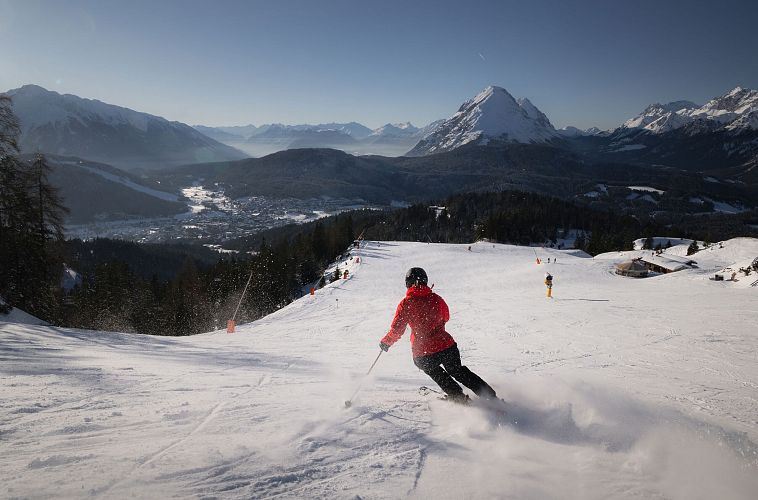 Sciatore in giacca rossa su una pista da sci con montagne sullo sfondo.