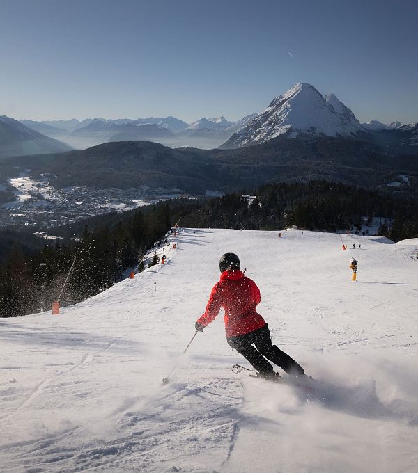 A skier in a red jacket skiing down a snowy slope with mountains in the background.