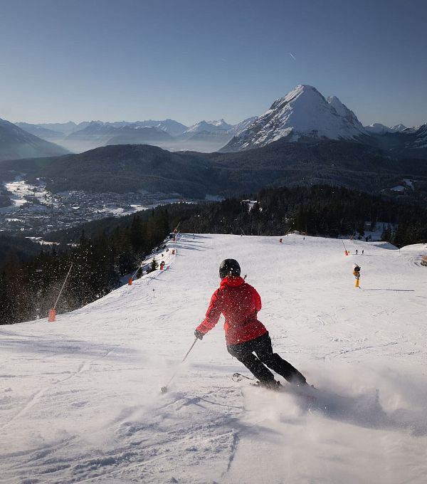 A skier in a red jacket skiing down a snowy slope with mountains in the background.