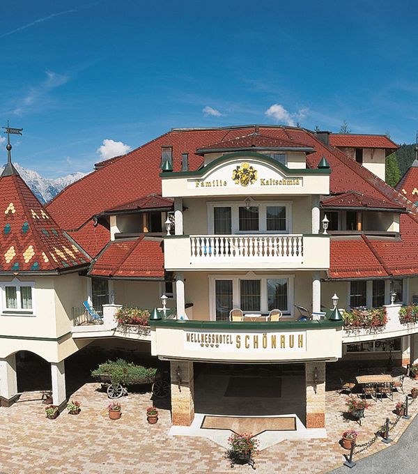 Charmantes Gebäude mit rot gefliesten Dächern, umgeben von Wiesen und blauem Himmel.