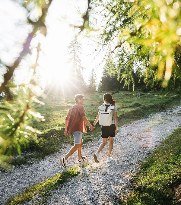 Ein Paar geht Hand in Hand auf einem Weg durch eine sonnige Landschaft.