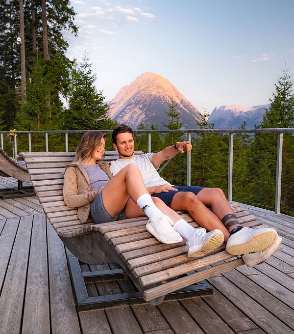 Sonnenaufgang Aussichtsplattform Bruschkopf - Paar lieht auf Holzliege auf der Plattform - Mann zeigt auf etwas