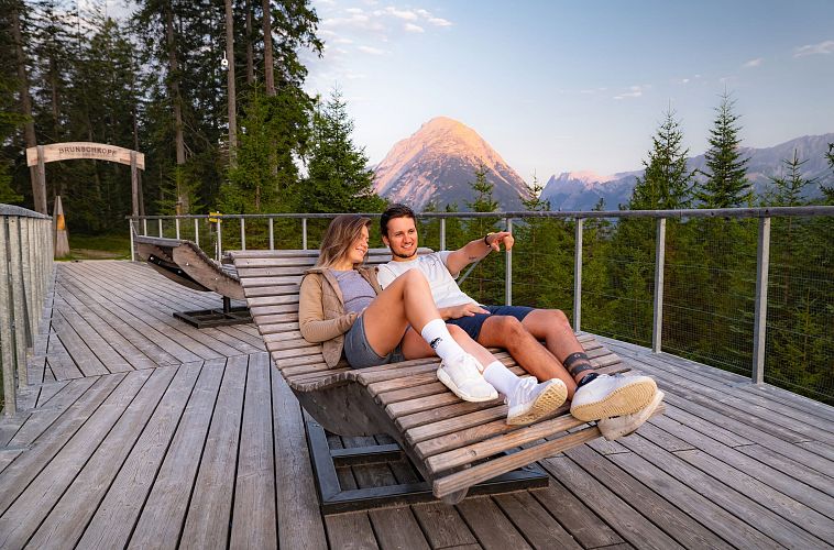 sonnenaufgang-aussichtsplattform-bruschkopf-paar-lieht-auf-holzliege-auf-der-plattform-mann-zeigt-auf-etwas