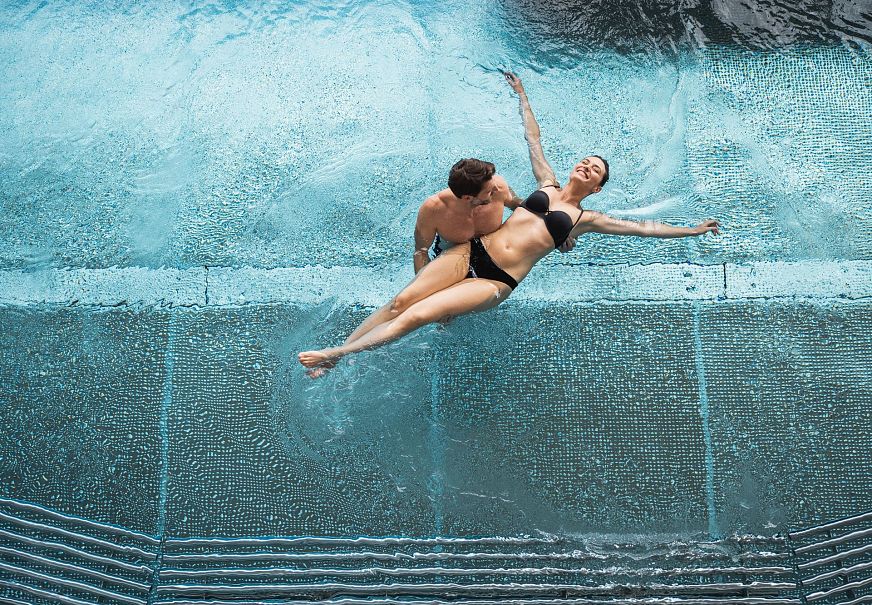 A couple swimming playfully in a clear blue pool.