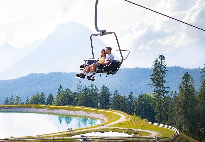 A couple on a chairlift with a lake and mountains in the background.