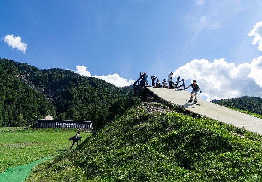 A skateboard ramp with people at the top and one individual boarding down.