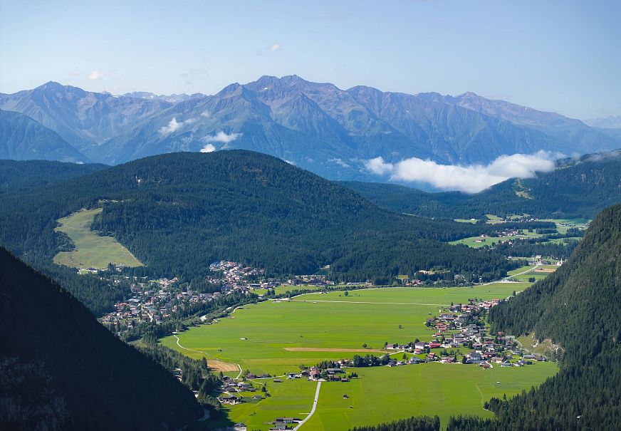 Aussicht auf ein grünes Tal mit Bergen im Hintergrund und kleinen Dörfern.