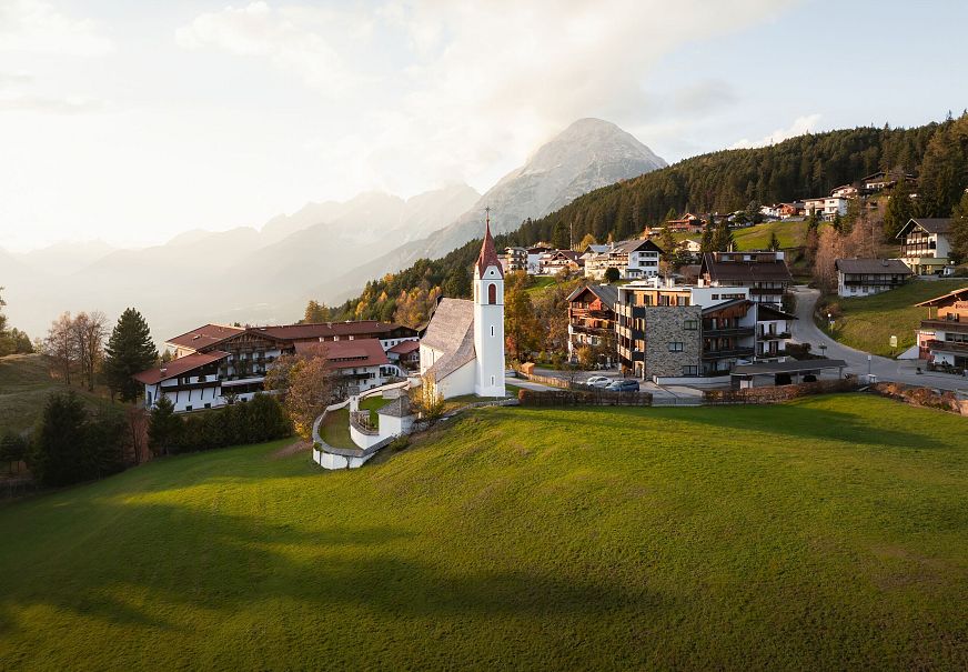 Ein Ort mit einem Kirchturm, Hügeln und Bergen in der Umgebung.