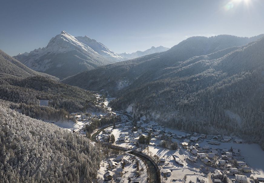 Winterlandschaft mit schneebedeckten Bergen und einem kleinen Dorf in der Talebene.