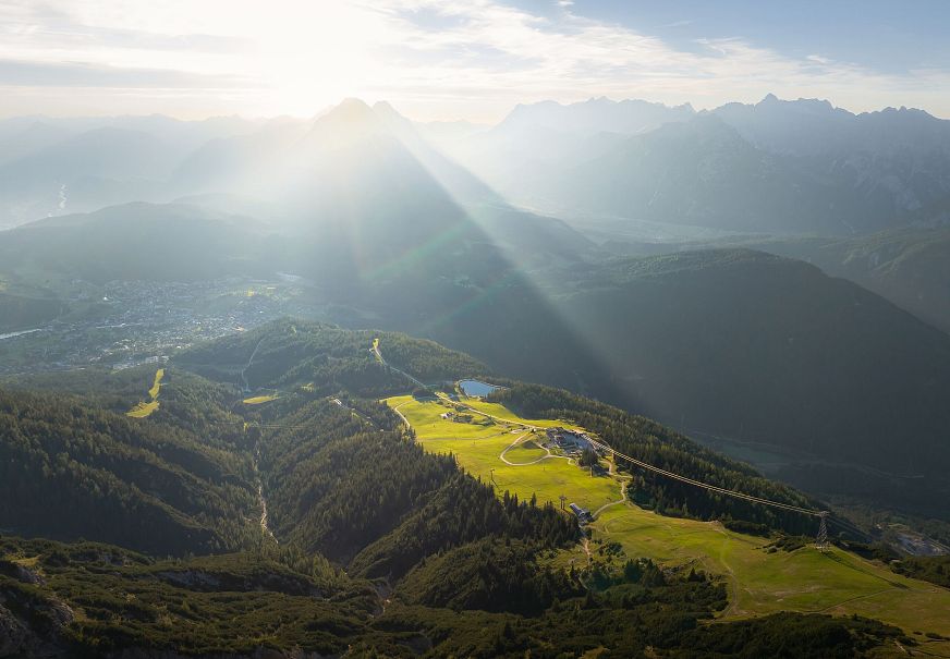 Berglandschaft mit Wiesen und Gipfeln, Sonnenstrahlen durchbrechen die Wolken.