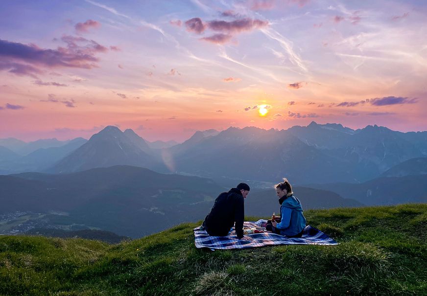 Ein Paar sitzt beim Sundowner Picknick mit Blick Richtung Leutasch