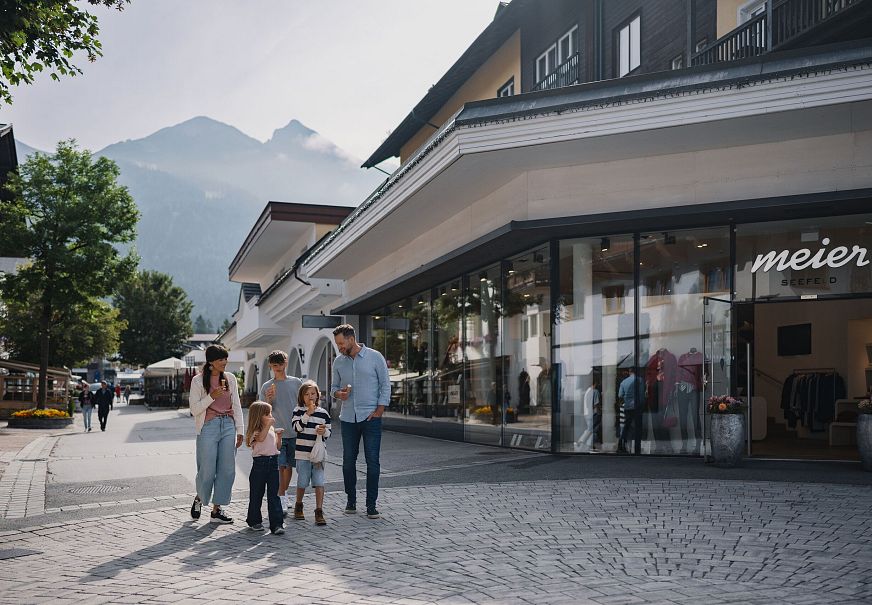 A family walking along a street with shops, surrounded by mountains.