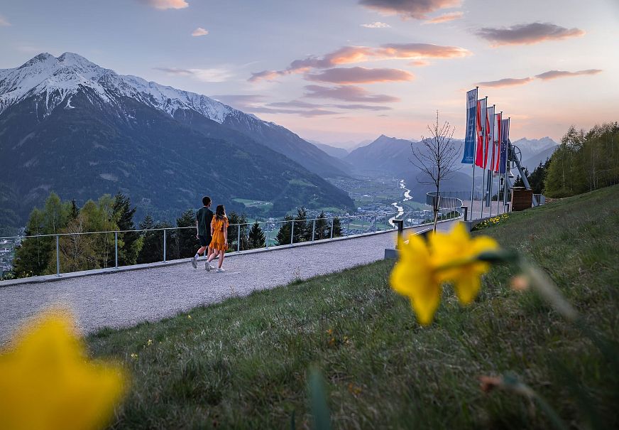 Friedensglocke Mösern zur Sonnenuntergangsstimmung im Frühling - Paar läuft zur Glocke mit Blumen im Vordergrund