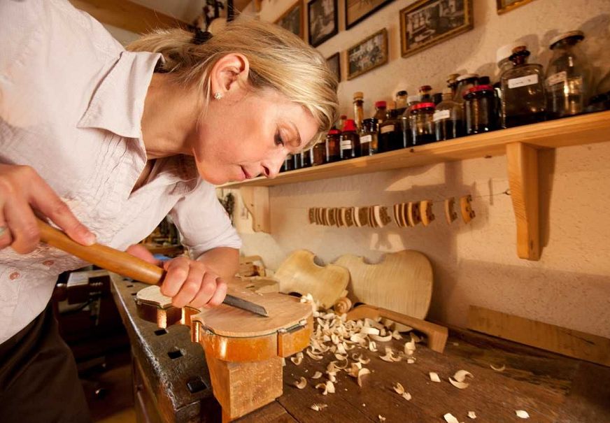 A woman carving wood in a workshop filled with tools and materials.