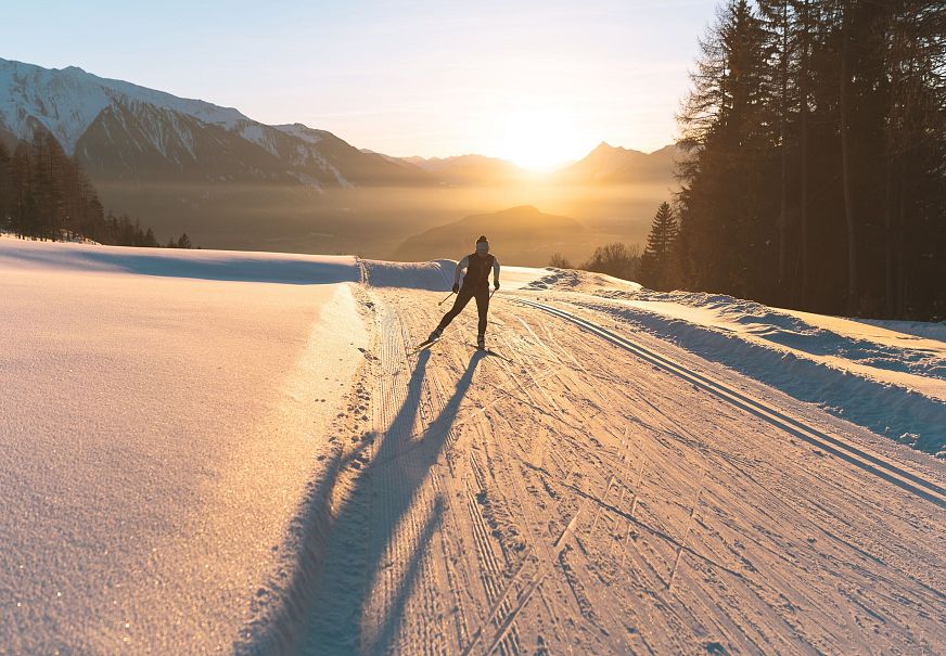 Langläufer bei Sonnenuntergang in der Region Seefeld, umgeben von Bergen und verschneiter Landschaft.