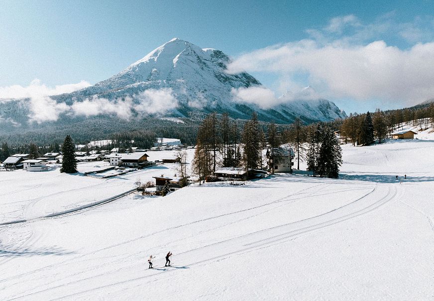 Zwei Langläufer in der Region Seefeld, umgeben von verschneiten Bergen und Wald.