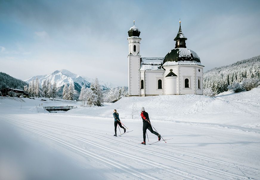 Langläufer vor Kirche in schneebedeckter Landschaft der Region Seefeld. Ideal zum Langlaufen.
